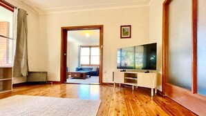 Uma sala de estar com piso de madeira, uma televisão e uma porta que dá para outro cômodo.