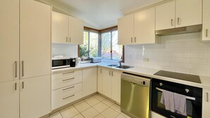 Cozinha moderna com armários brancos, máquina de lavar louça, forno e janela que oferece luz natural.