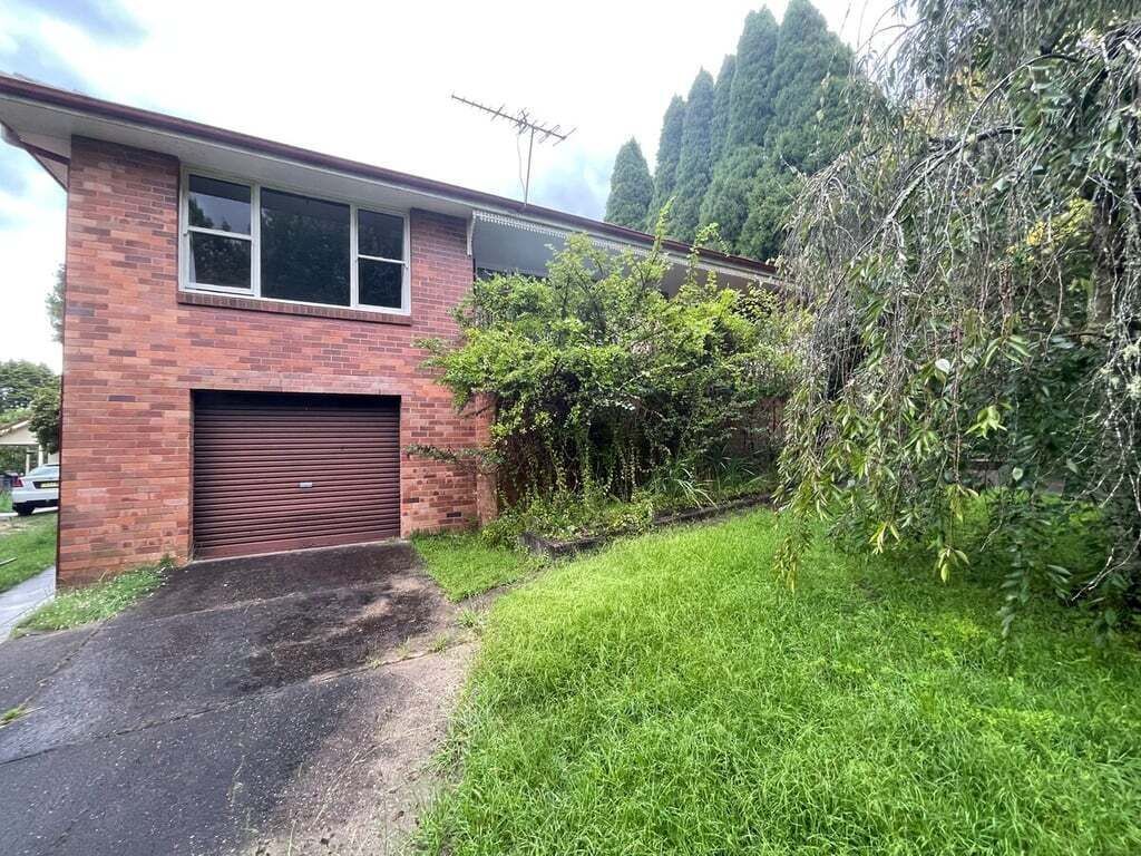 A single-story brick house with a garage, a small front yard with grass, and a tree to the right.
