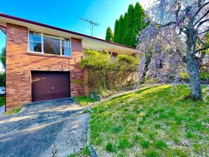A two-story brick house with a garage, a driveway, and a tree with purple flowers.