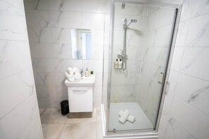 A modern bathroom with a glass-enclosed shower, white marble tiles, a sink with toiletries, and a mirror.