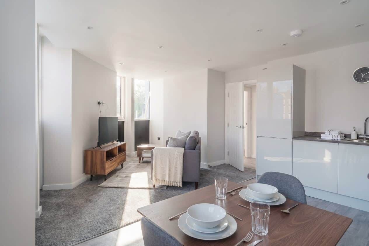 A modern living space with a dining area, a sofa, a television, and a kitchen area.
