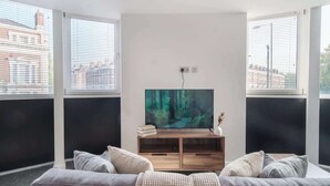 Un soggiorno moderno con un'ampia TV a schermo piatto, un mobile TV in legno e un divano grigio.
