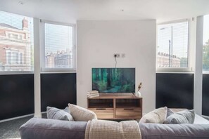Una sala moderna con un televisor de pantalla plana grande, un mueble de entretenimiento de madera y un sofá gris.