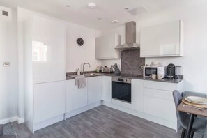 Una cocina moderna con armarios blancos, horno empotrado, microondas y cafetera.