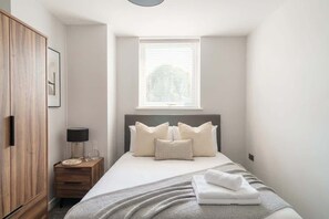 A bedroom with a bed, a bedside table, a lamp, a window, and a wardrobe.