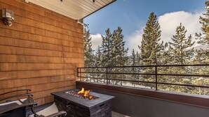 Eine Holterrasse mit einem Steinkamin und Blick auf schneebedeckte Bäume.