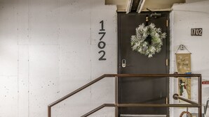 Eine Treppe mit Metallgeländer, eine schwarze Tür mit einem Kranz und die Zahl '1702' an der Wand.