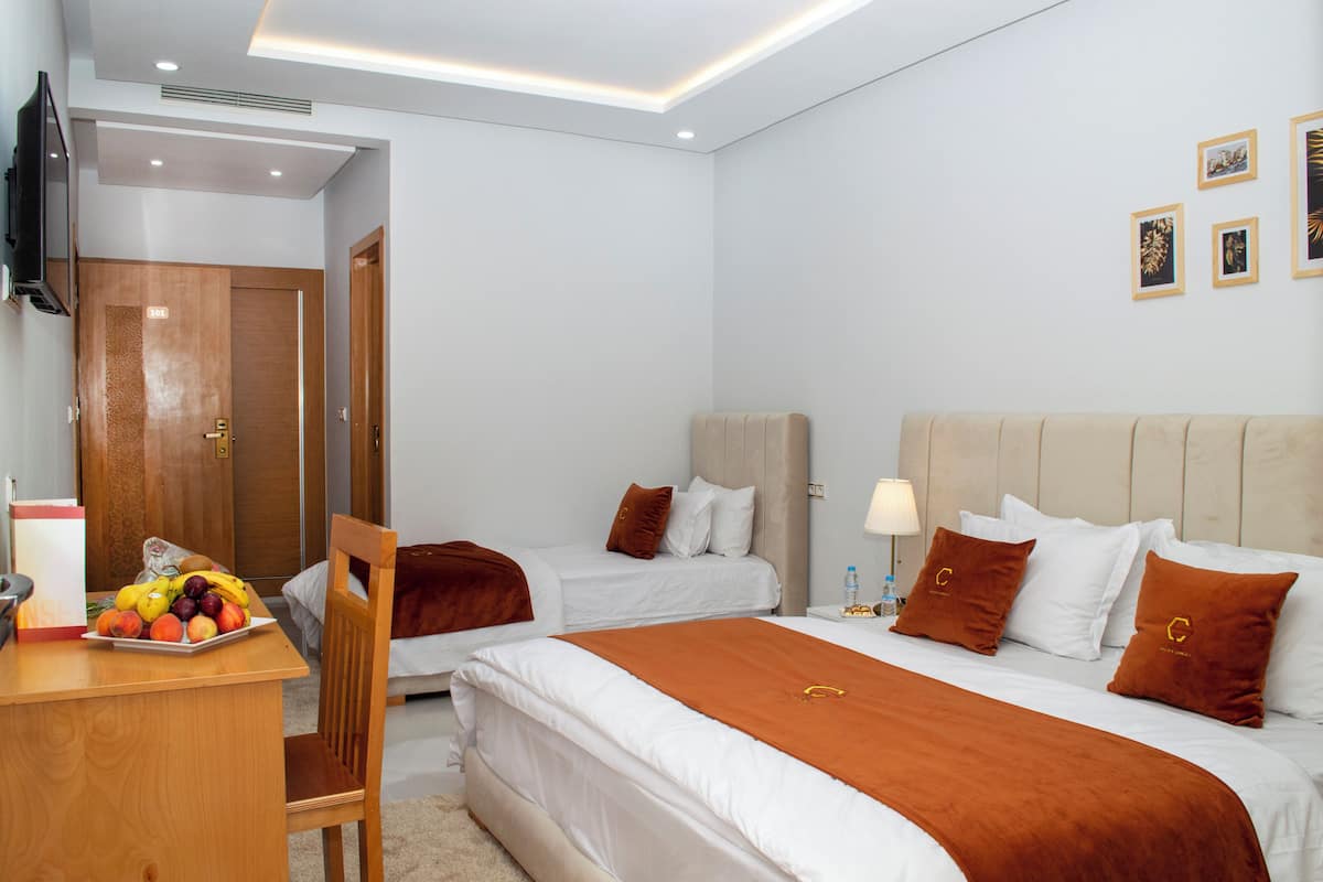 Une chambre d’hôtel avec deux lits, un bureau avec des fruits, une télévision et une porte.