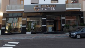 Ein mehrstöckiges Hotel mit Balkonen, Klimaanlagen und einem Schild mit der Aufschrift 'Golden Sunset Hotel'.
