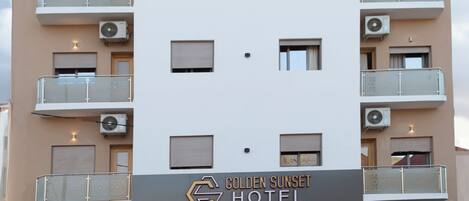 Een meerlaags hotel met balkons, airconditioning en een bord met de tekst 'Golden Sunset Hotel'.