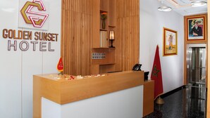 Ein Hotelrezeptionstresen mit einer Wandverkleidung aus Holz, einem Schild mit der Aufschrift 'Golden Sunset Hotel', einer roten Flagge und einem gerahmten Gemälde an der Wand.