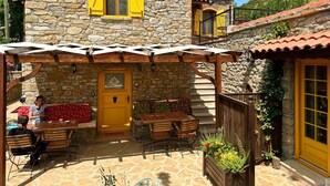 A stone building with a yellow door and shutters, a covered patio with wooden furniture, and a small balcony. - Ilios Gokceada (Gökçeada)