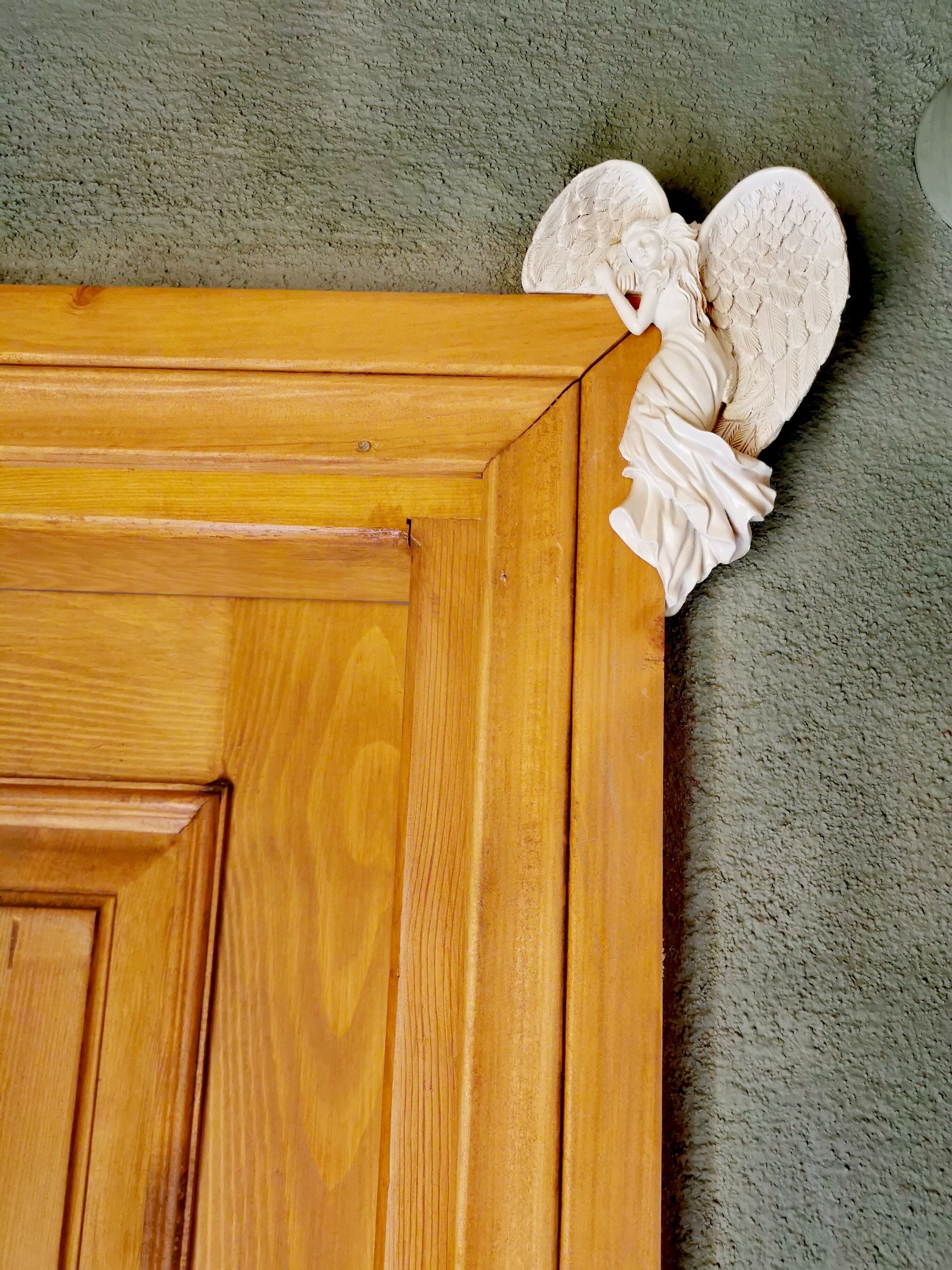 Une porte en bois ornée d’une sculpture d’ange dans le coin supérieur.
