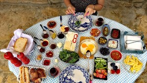A round table with a checkered tablecloth, filled with various dishes, including bread, cheese, olives, and a glass of red wine. - Ilios Gokceada (Gökçeada)