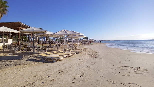 Une plage avec des parasols et des chaises longues, un ciel dégagé et l’océan.