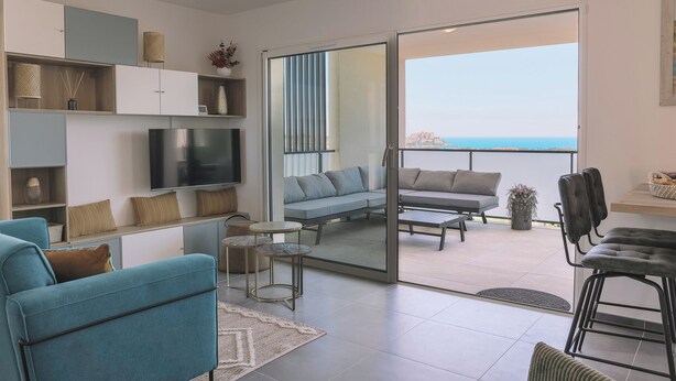 Un salon moderne avec un téléviseur, un canapé et un balcon offrant une vue sur la mer.