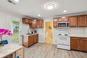 A compact kitchen with wooden cabinets, a white stove, a microwave, and a sink.