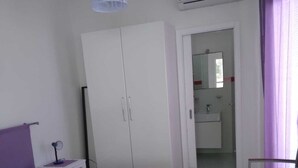 A bedroom with a bed, wardrobe, bedside table, and a bathroom visible through an open door. - Vignamarino House (Alessano)