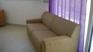 A beige sofa in a room with a window, a flat-screen TV mounted above it, and a telephone on the wall. - Vignamarino House (Alessano)