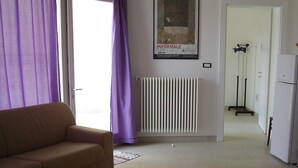 A living room with a sofa, a radiator, a poster on the wall, and a door leading to another room. - Vignamarino House (Alessano)