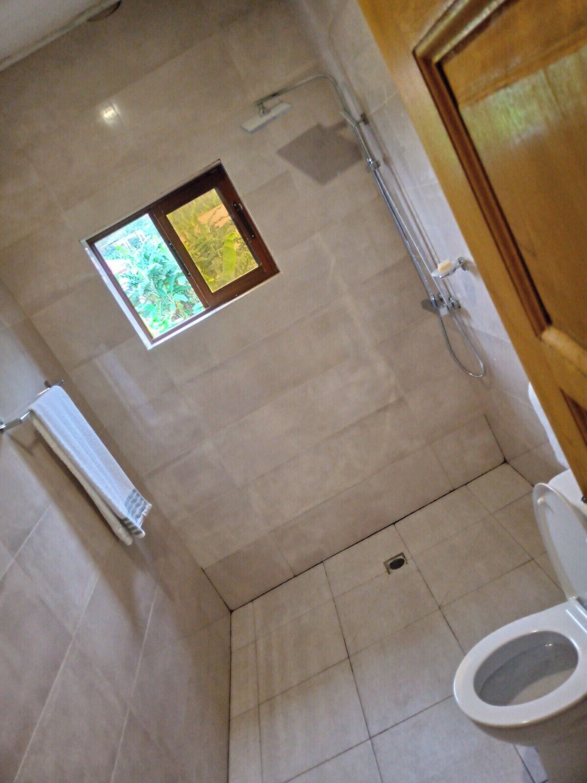 A bathroom with a shower, a toilet, and a small window with a view of greenery.