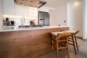 A modern kitchen with a central island, stainless steel appliances, and wooden bar stools. - Luxury 3 bedroom Apartment at the beach (Punta Cana)