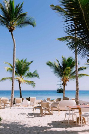 Una playa con palmeras, sillas y una mesa lista para comer.