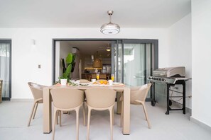 A dining area with a table and chairs, a grill, and a view of the kitchen. - Luxury 3 bedroom Apartment at the beach (Punta Cana)