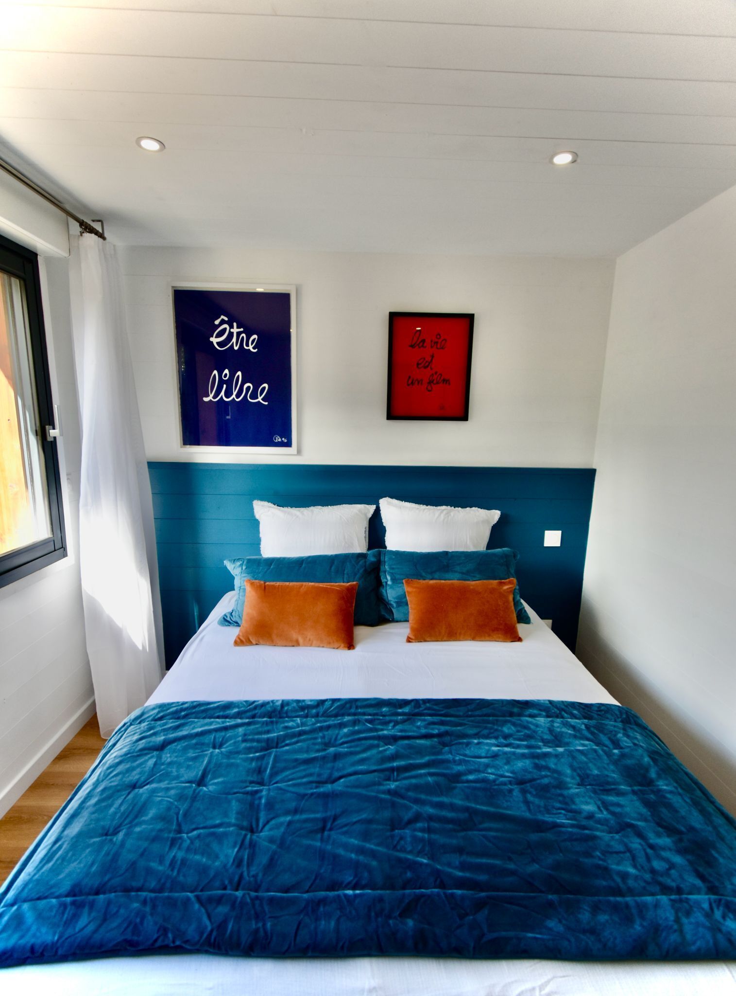 Une chambre moderne avec une t ête de lit bleue, un grand lit avec une literie bleue et orange, et deux œuvres d’art murales.