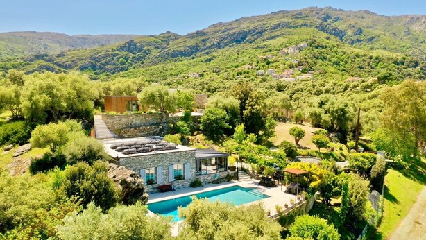 Eine Villa mit Swimmingpool, umgeben von  üppiger Vegetation und Hügeln im Hintergrund.