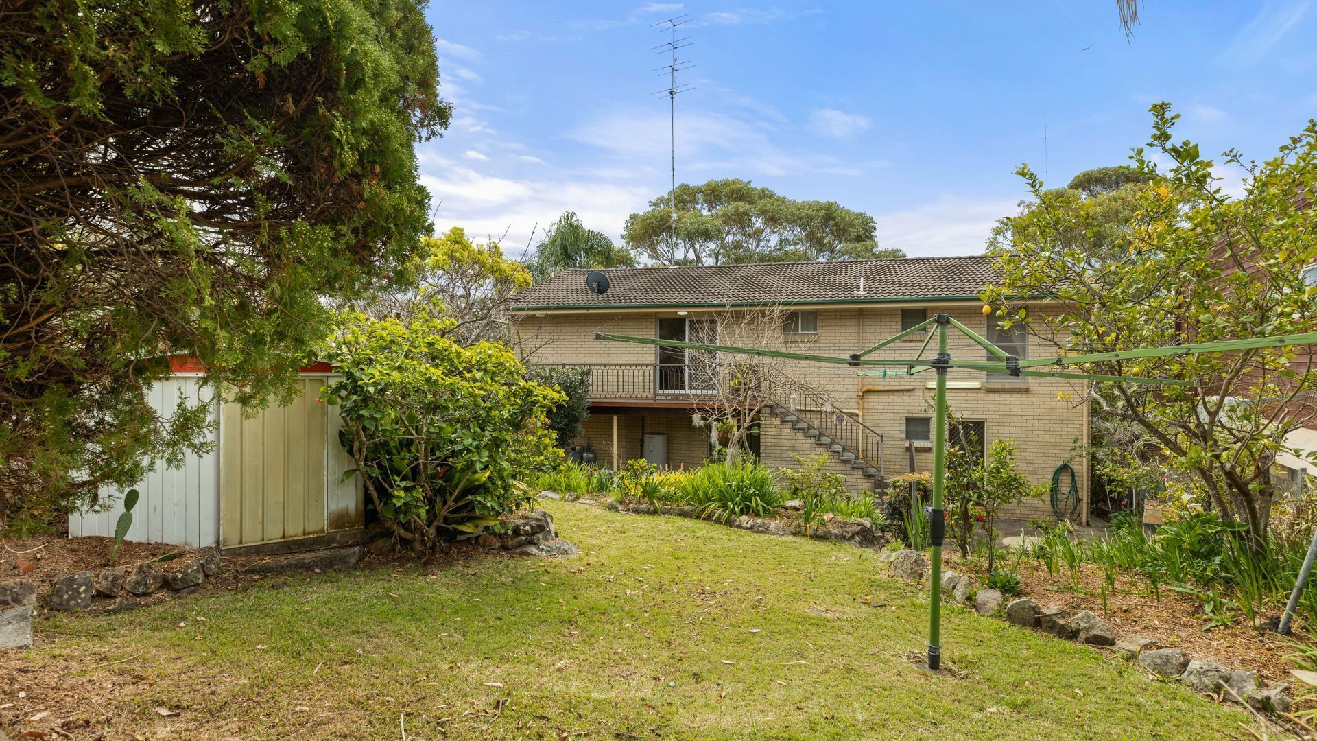A two-story house with a front yard, a satellite dish, and a green metal structure.