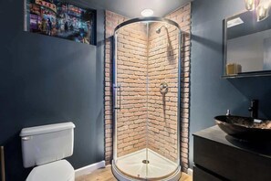 Ein modernes Badezimmer mit Duschkabine aus Glas, einer weißen Toilette und einem schwarzen Waschbecken mit großem Becken.