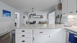 A modern kitchen with white cabinetry, a marble countertop, and a hanging light fixture. - Calling All Gamers_Sleeps 10_Near MCI_Fun for All (Platte City)