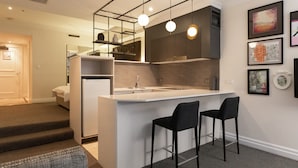 Cocina compacta con isla central, dos taburetes de bar e iluminación colgante moderna.