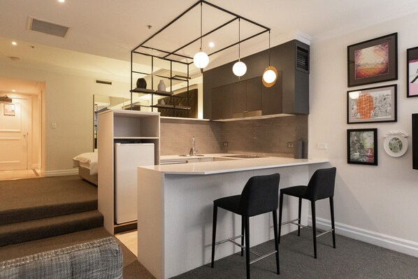 A compact kitchen with a central island, two bar stools, and modern pendant lighting.