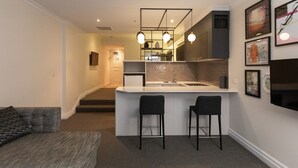 Una cocina moderna con encimera blanca, dos taburetes de bar e iluminación colgante.