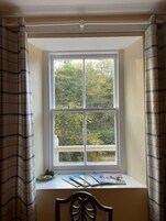 Una ventana con vistas a un bosque, un alféizar con revistas y una silla.