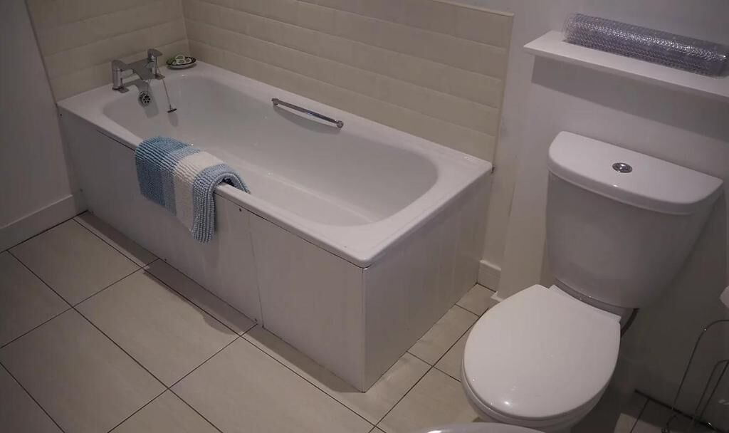 A bathroom with a bathtub, toilet, and tiled floor.