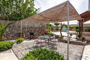 An outdoor patio with a stone wall, a barbecue grill, and a table with chairs. - Joel Living Collection - Rustic Villa (Chania)