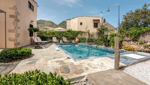 Ein Pool mit Steinplatten, Liegestühlen und einem Berg im Hintergrund.