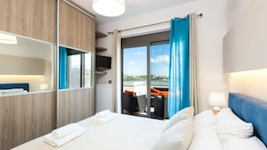 Ett hotellrum med en stor säng, utsikt över omgivningarna, en balkong med sittplatser och en garderob i trä.