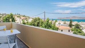 Un balcón con mesa y sillas, con vistas a un pueblo costero con edificios y cielo despejado.