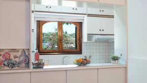 A kitchen with white cabinets, a window with a view of greenery, a sink, and a fruit bowl.