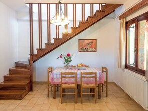 A dining area with a wooden staircase, a table with a floral tablecloth, and a vase with flowers. - Romantic Corner - Penelope Sea View Maisonette (Stalos)