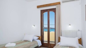 A room with two beds, a view of the sea through a glass door, and a radiator on the wall.