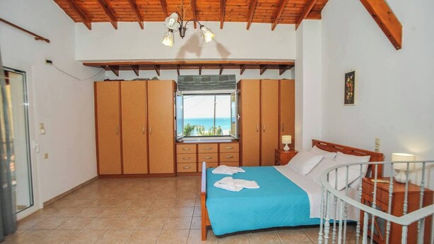 A bedroom with a bed, a window with a view, wooden wardrobes, and a ceiling with exposed beams. - Romantic Corner | Theofilos Sea View (Stalos)
