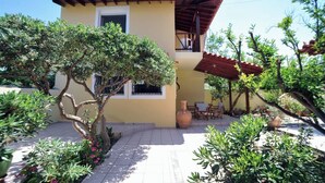 A two-story house with a tiled patio, a covered outdoor seating area, and a variety of plants. - Romantic Corner | Theofilos Sea View (Stalos)