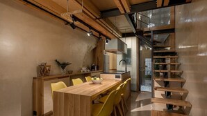 A modern kitchen with a wooden island, yellow chairs, and a staircase with wooden steps. - Casa Sorvolou Boutique House (Chania)