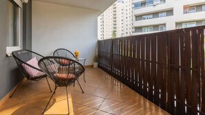 A balcony with two black wire-framed chairs, a small table with a vase of flowers, and a dark wooden fence.